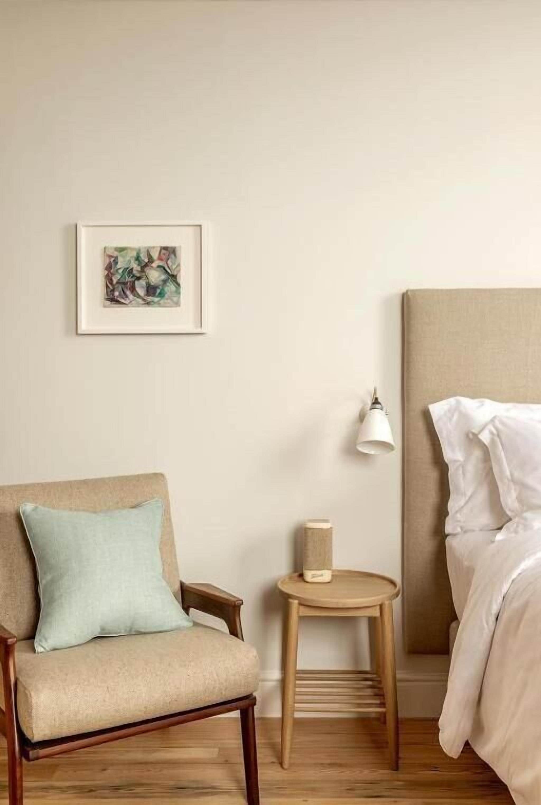 A bedroom with a bed, a chair, a small table, a lamp, and a framed picture on the wall.