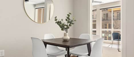 A dining area with a round mirror, a vase with greenery, and white chairs around a dark wooden table.