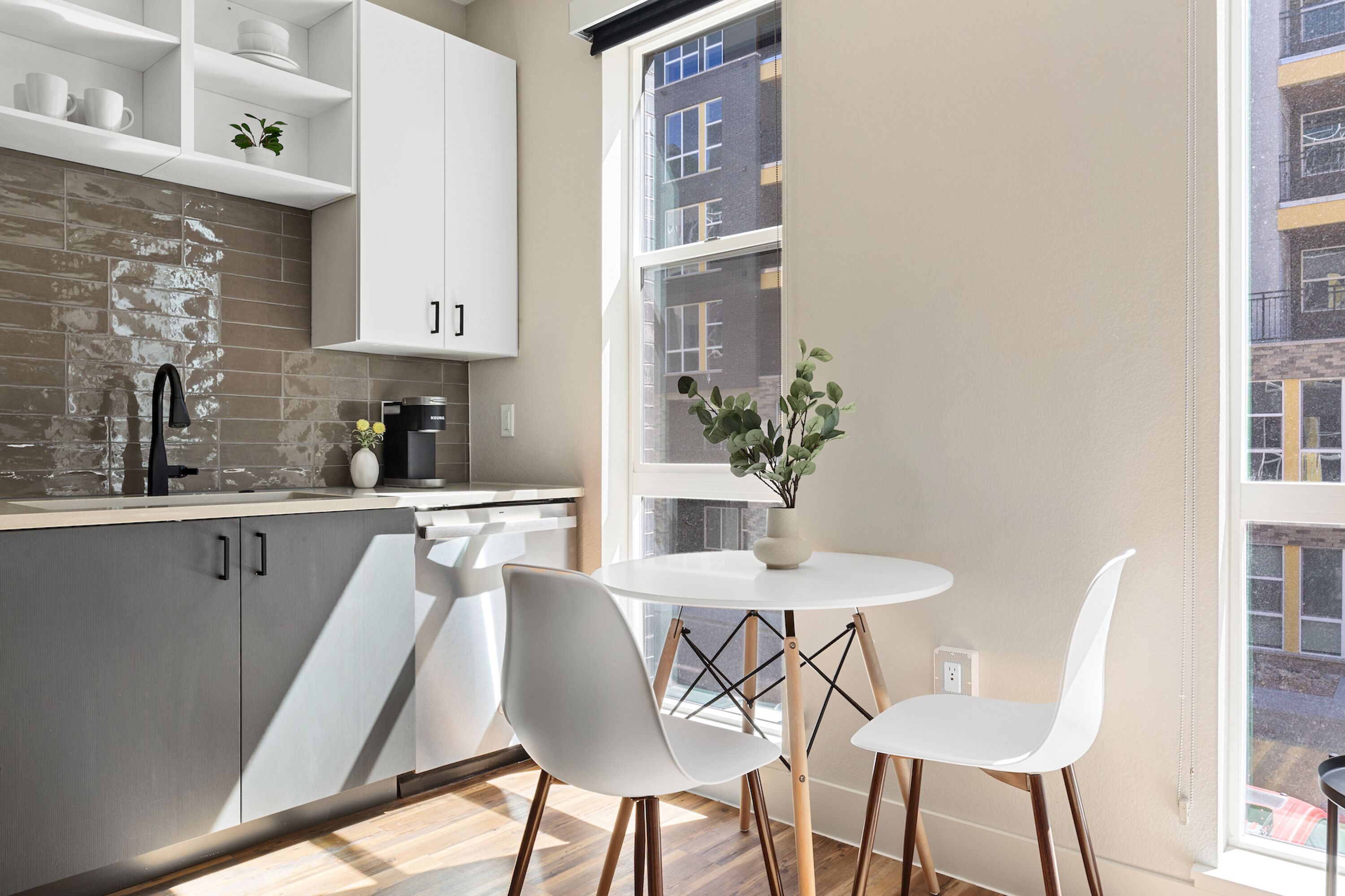 A modern kitchen with white cabinets, a round dining table, and two white chairs.