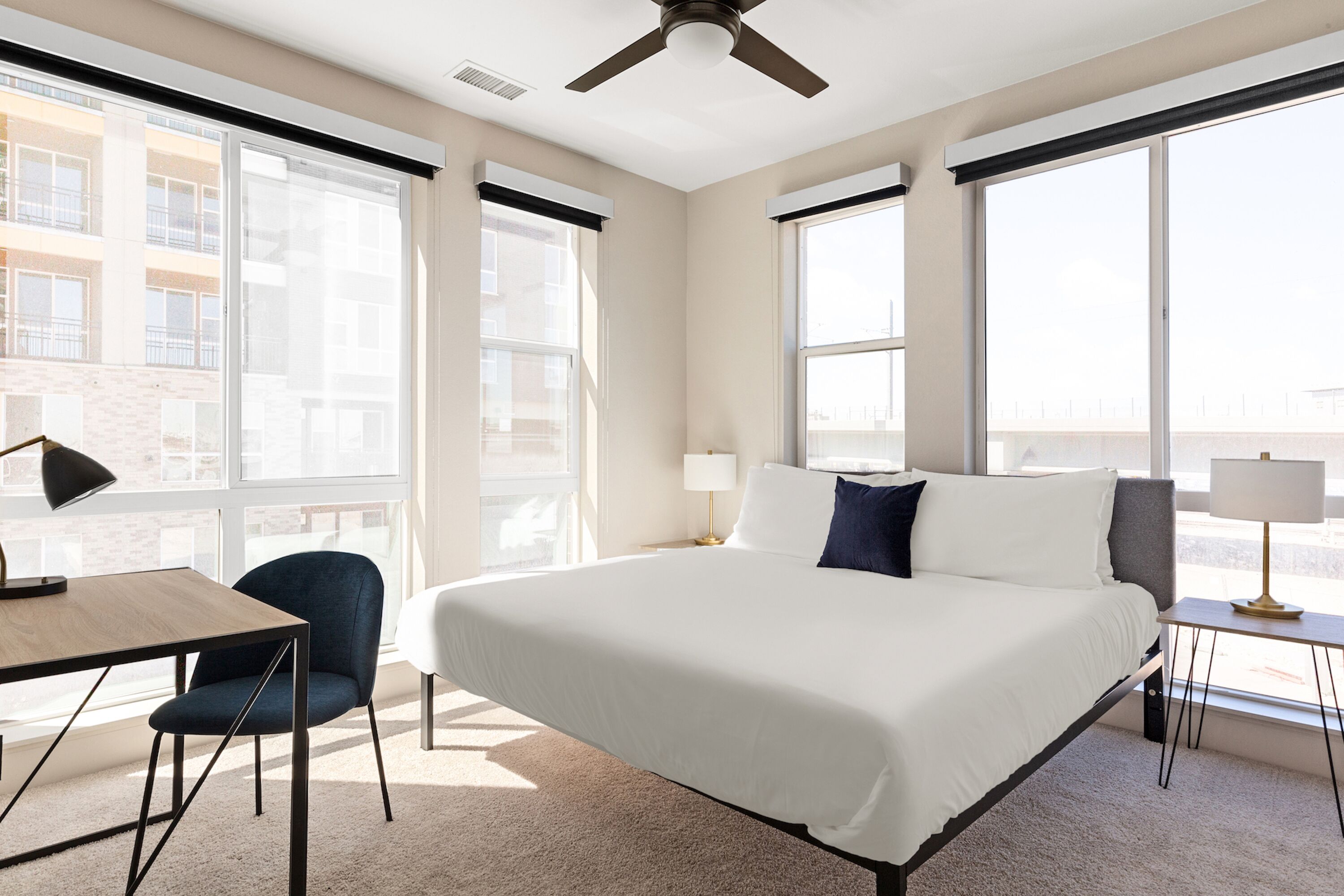 A hotel room with a large bed, a desk, a chair, and a window with a view of buildings.