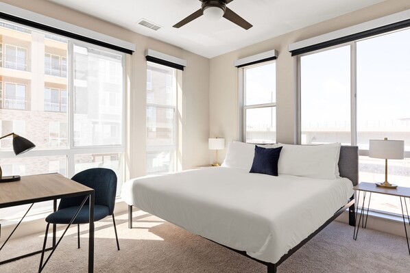 A hotel room with a large bed, a desk, a chair, and a window with a view of buildings. - Kasa Rino Denver (Denver)