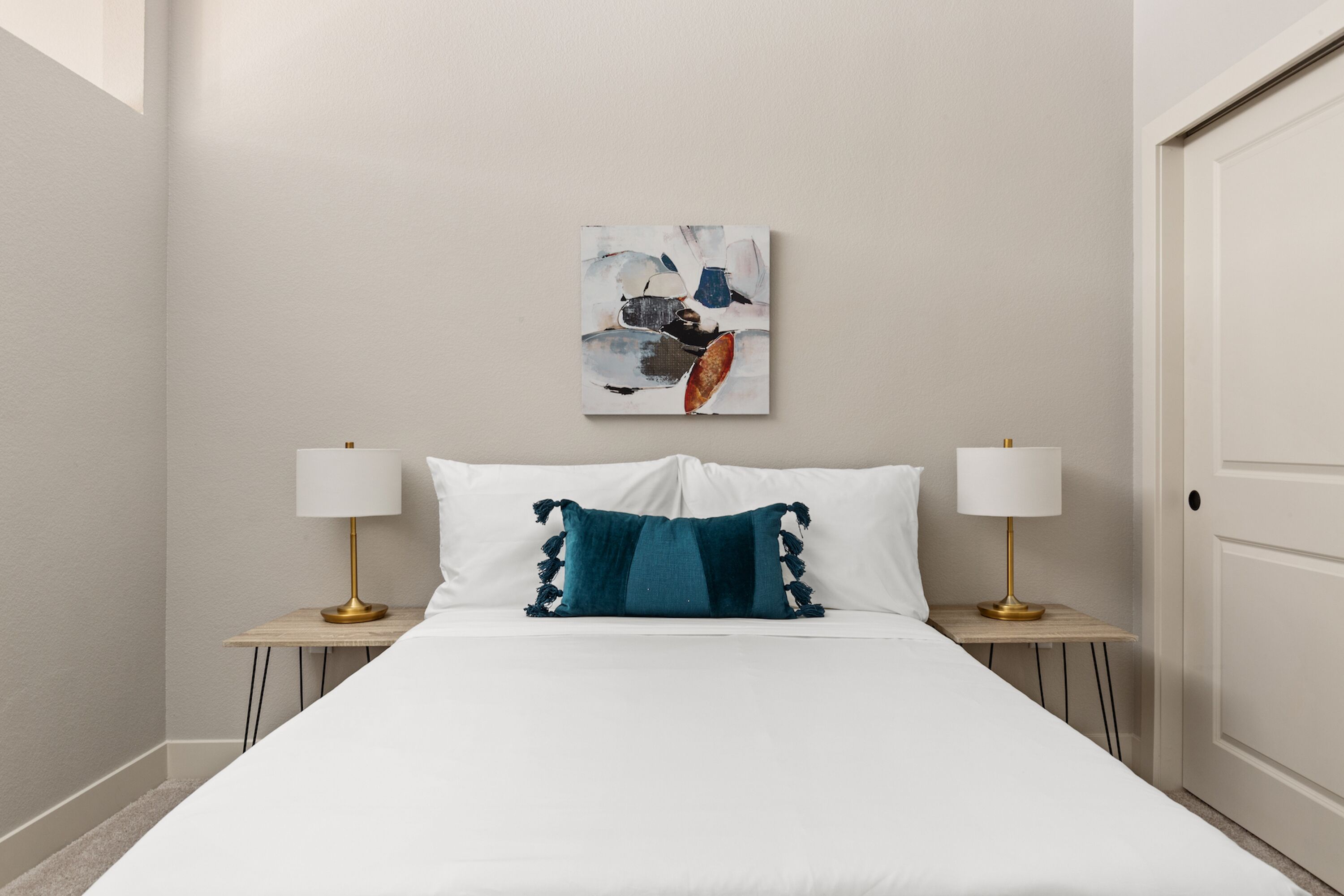A hotel room with a large bed, two bedside tables with lamps, a wall-mounted artwork, and a door.