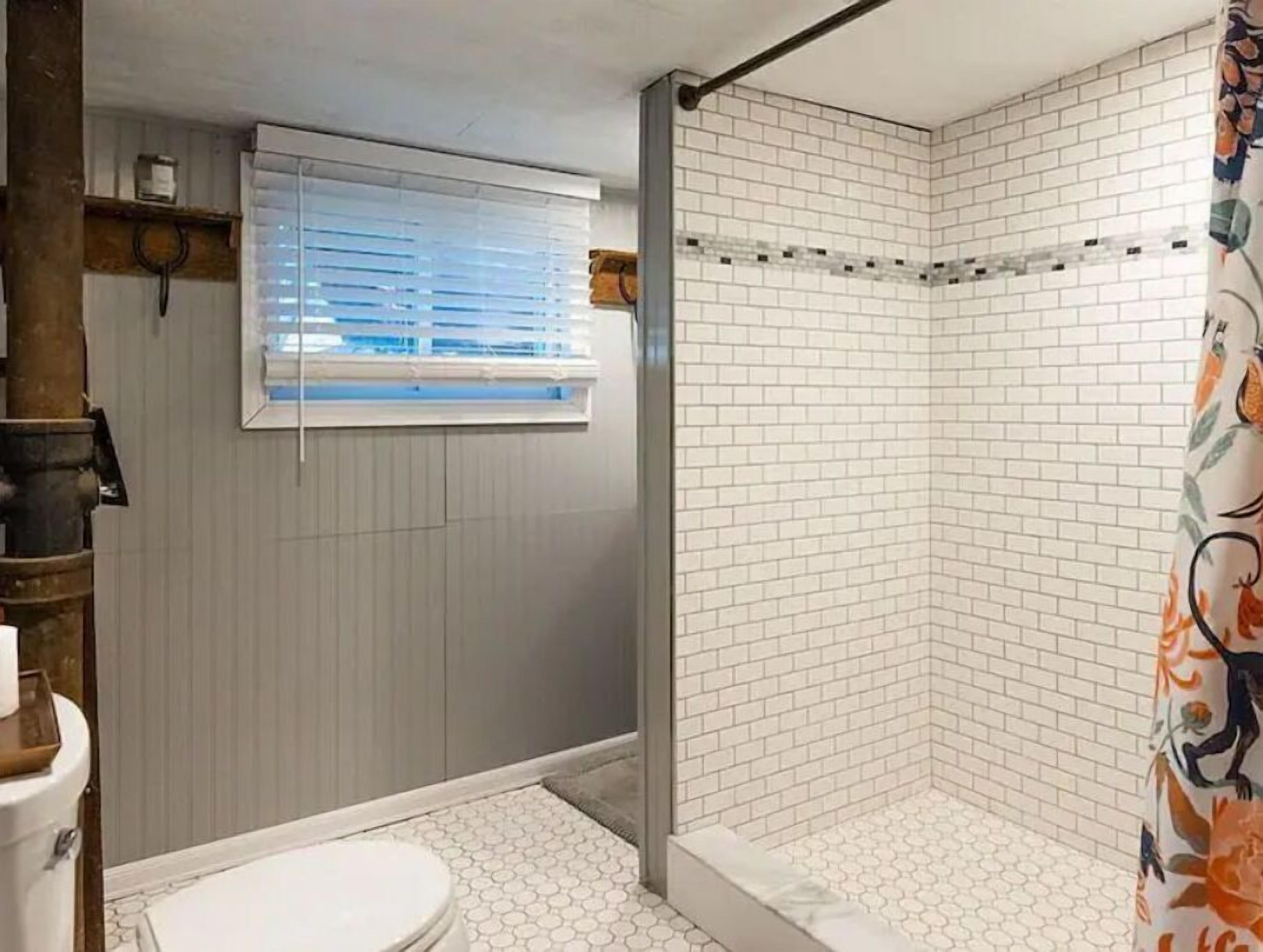 Een badkamer met douche, toilet en raam.