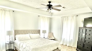 Ein Hotelzimmer mit einem großen Bett, zwei Nachttischen mit Lampen, einem Deckenventilator und einer dunklen Holzkommode.