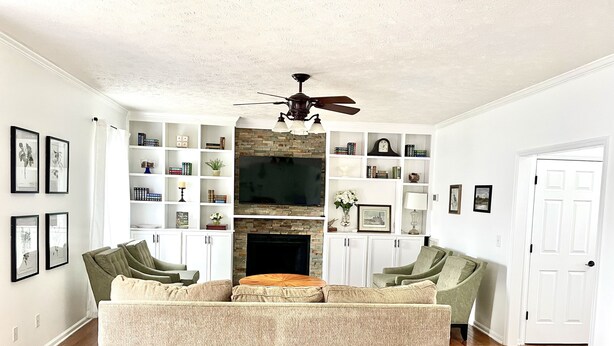 Ein Wohnzimmer mit einem Ecksofa, einem Kamin, einem Fernseher und einem Bücherregal.