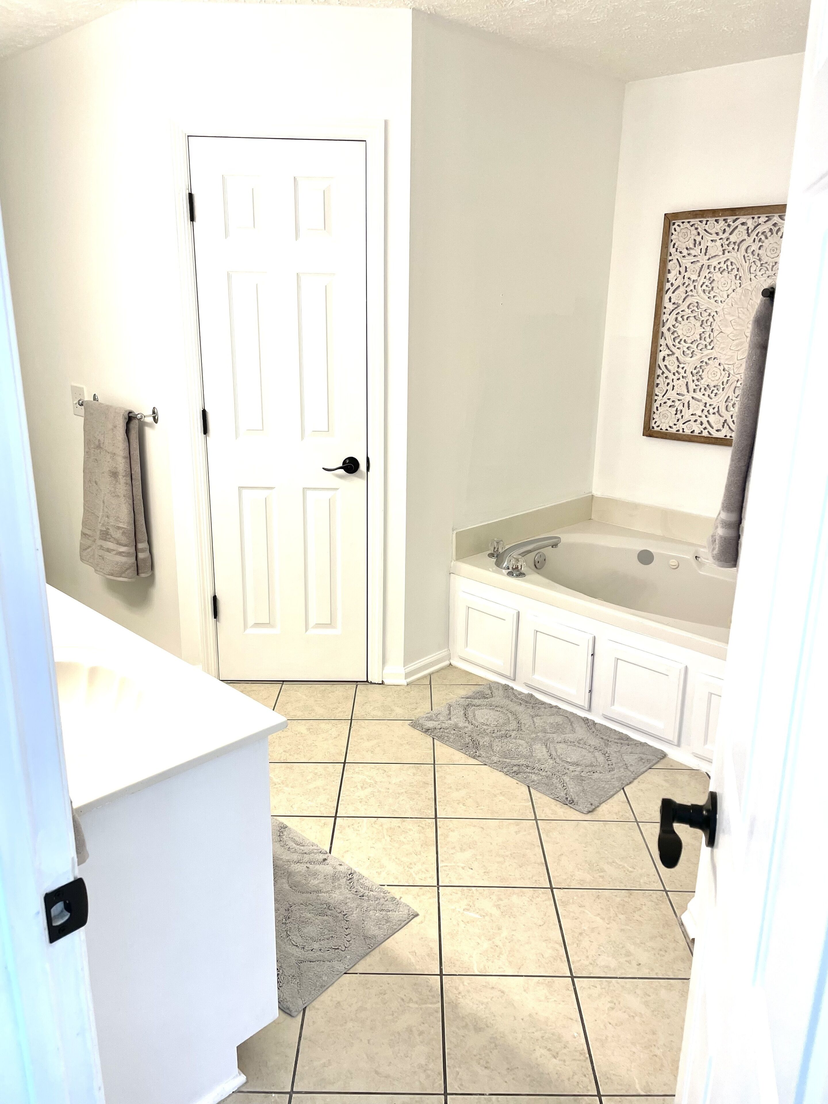 A bathroom with a white door, a bathtub, and a gray rug on the floor.