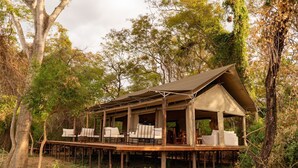 Una cabaña de madera con terraza cubierta, rodeada de árboles.