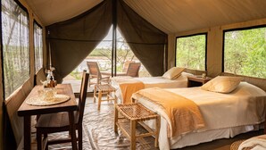 Alojamiento tipo carpa con dos camas, una mesa con sillas y vista a zonas verdes.
