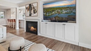 Una sala de estar moderna con chimenea, un televisor de pantalla plana grande montado en un mueble blanco y un rincón de estar acogedor con un tapete a rayas.