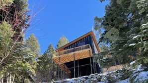 Ein modernes Gebäude mit einem Holzbalkon, umgeben von schneebedeckten Bäumen und Felsen.