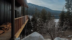 Eine Holzjagdhaus mit einer Terrasse mit Blick auf eine Berglandschaft und einen See.