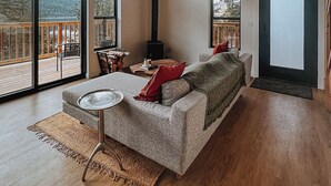 Un salon spacieux avec un grand canapé, une table basse et une cheminée. La pièce est dotée de grandes fenêtres et d’un plafond en bois.