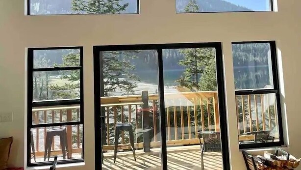 Une pièce spacieuse dotée de grandes fenêtres donnant sur une terrasse et sur les montagnes.