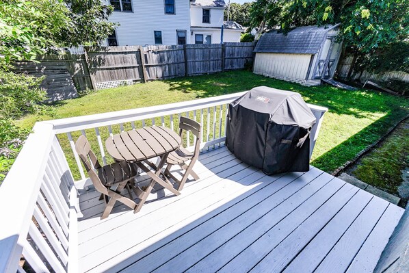 Une terrasse en bois avec une table et des chaises, un couvercle pour barbecue et une cour arrière clôturée.