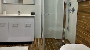 Uma casa de banho moderna com cabine de chuveiro em vidro, toucador de madeira e um espelho grande.