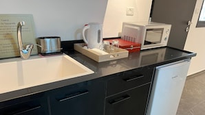 Cozinha moderna com bancada preta, pia de aço inoxidável, micro-ondas, chaleira e geladeira compacta.