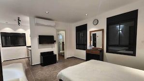 Quarto de hotel moderno com cama, escrivaninha, televisão e banheiro visível por uma porta aberta.
