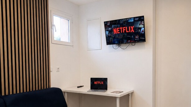 A modern living room with a sofa, a desk with a laptop, a mounted TV displaying the Netflix logo, and a wooden slatted wall. - Villa Berria, 9 Pool / BBQ / Your Oasis near Palma (Es Pont d`Inca)