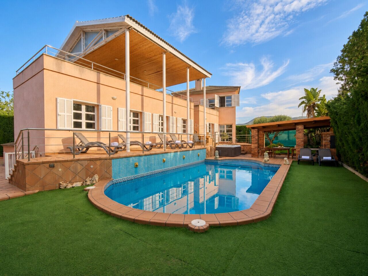 Een modern huis met een zwembad, een overdekt terras en een verzorgd gazon.