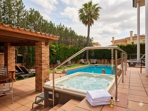 Uma banheira de hidromassagem com guarda-corpo de metal, piscina e espreguiçadeiras em um quintal.