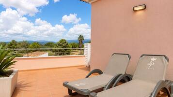 A terrace with two lounge chairs, a potted plant, and a view of the landscape.