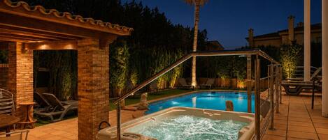 Área de jacuzzi y piscina con sillones de descanso y una pérgola.