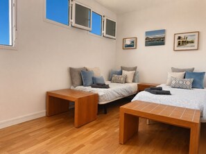 Quarto com duas camas, um banco de madeira e uma mesinha de cabeceira.