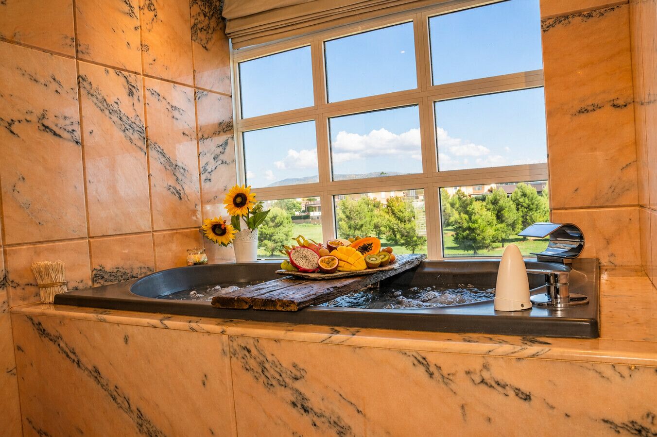 A bathroom with a marble wall, a window with a view of greenery, a sink with a fruit bowl, and a towel rack.