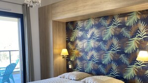 Un dormitorio espacioso con una cama grande, una araña, un cabecero de madera y un papel tapiz con motivos de hojas tropicales.