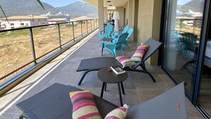 Un balcón con sillones de descanso, una mesa y vistas a un crucero y montañas.