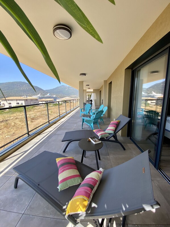A balcony with lounge chairs, a table, and a view of a cruise ship and mountains. - VERY LARGE NEW APARTMENT 300 m from the beach, SUPERB OCEAN VIEW, sleeps 6–8 (Propriano)