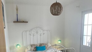 A bedroom with a white metal bed frame, a wooden floor, a small bedside table with a lamp, and a hanging light fixture. - Estrela do Atlântico (Açores)