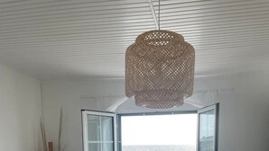 A modern living room with a large window offering a view of the sea, a cozy sofa, a small round table with a plant, and a hanging light fixture. - Estrela do Atlântico (Açores)