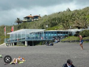 A beachside building with a glass facade, a covered walkway, and a hillside backdrop.