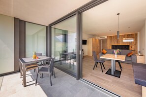 A modern living space with a glass sliding door leading to a dining area with a table and chairs, a sofa, and a wooden accent wall. - moderne Ferienwohnungen in Algund, Panoramablick und Pool am Algunder Waalweg (Algund)