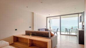 A modern living room with a wooden bench, a sofa, and a dining area with a view of the ocean.