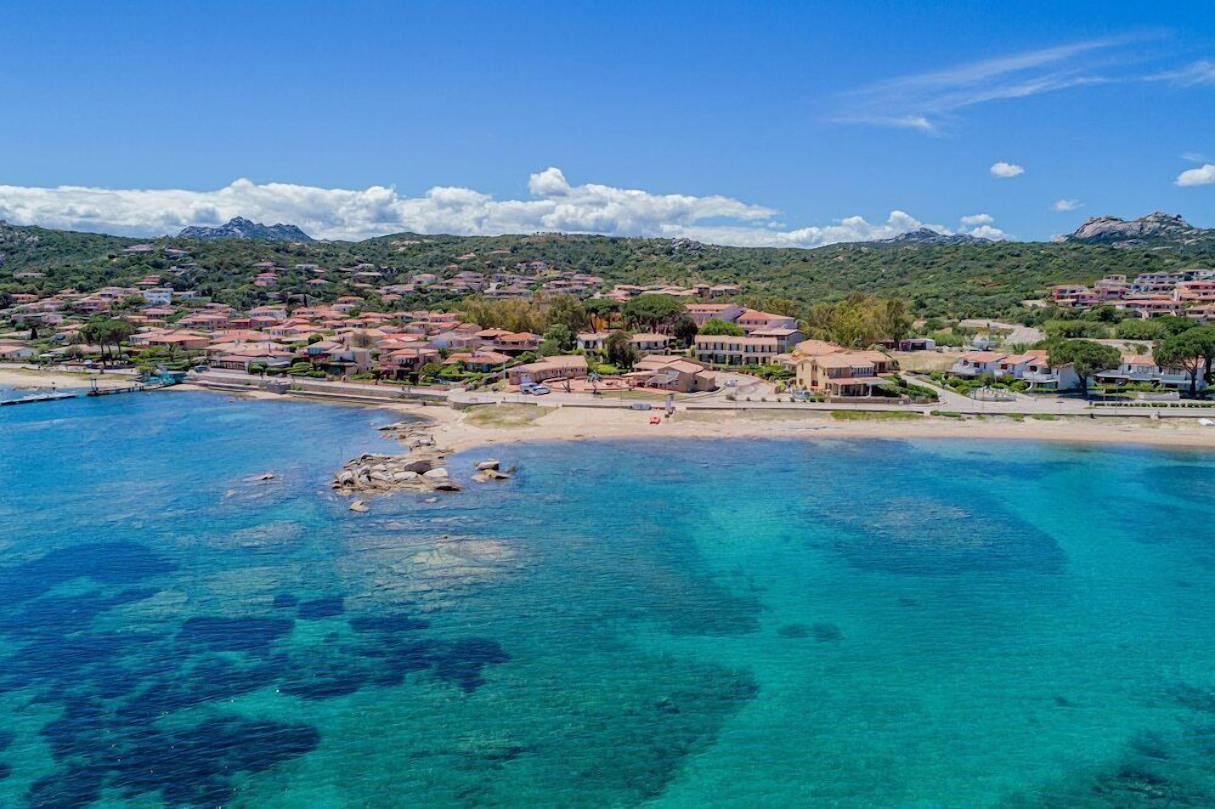 Una località costiera con acque blu cristalline, spiagge sabbiose e edifici dai tetti rossi.