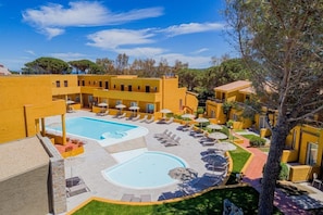 A hotel courtyard with two swimming pools, sun loungers, and a tree. - Blu Hotel Laconia (Arzachena)