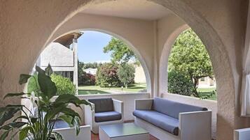 Area salotto esterna con divano, sedie e tavolino, incorniciata da archi e piante in vaso.
