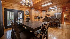 A wooden interior with a central island table, wooden cabinets, and a chandelier. - *Timber & Tin* Family Retreat~Creek~Arcade~Hot Tub (Suches)
