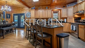 A wooden kitchen with a central island, a clock, and a sign reading "BAKERY". - *Timber & Tin* Family Retreat~Creek~Arcade~Hot Tub (Suches)