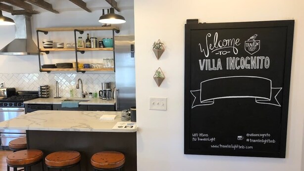 Une cuisine dotée d’un îlot en marbre, de tabourets de bar et d’une enseigne fixée au mur, accueillant les visiteurs à la Villa Incognito.