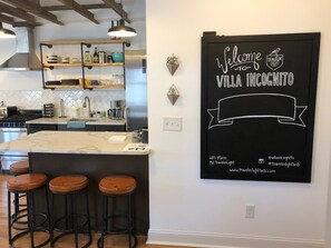 A kitchen with a marble island, bar stools, and a wall-mounted sign welcoming visitors to Villa Incognito.