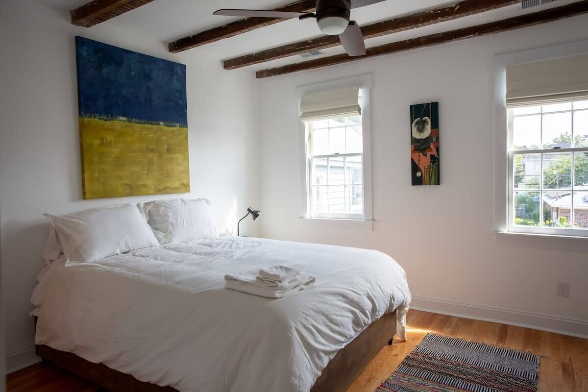 A bedroom with a large bed, wooden beams, a ceiling fan, and artwork on the walls.