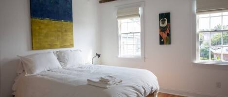 A bedroom with a large bed, wooden beams, a ceiling fan, and artwork on the walls.