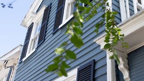 Un bâtiment à deux étages, avec un revêtement bleu et des bordures blanches, doté de nombreuses fenêtres avec volets et d’une antenne parabolique bien visible.