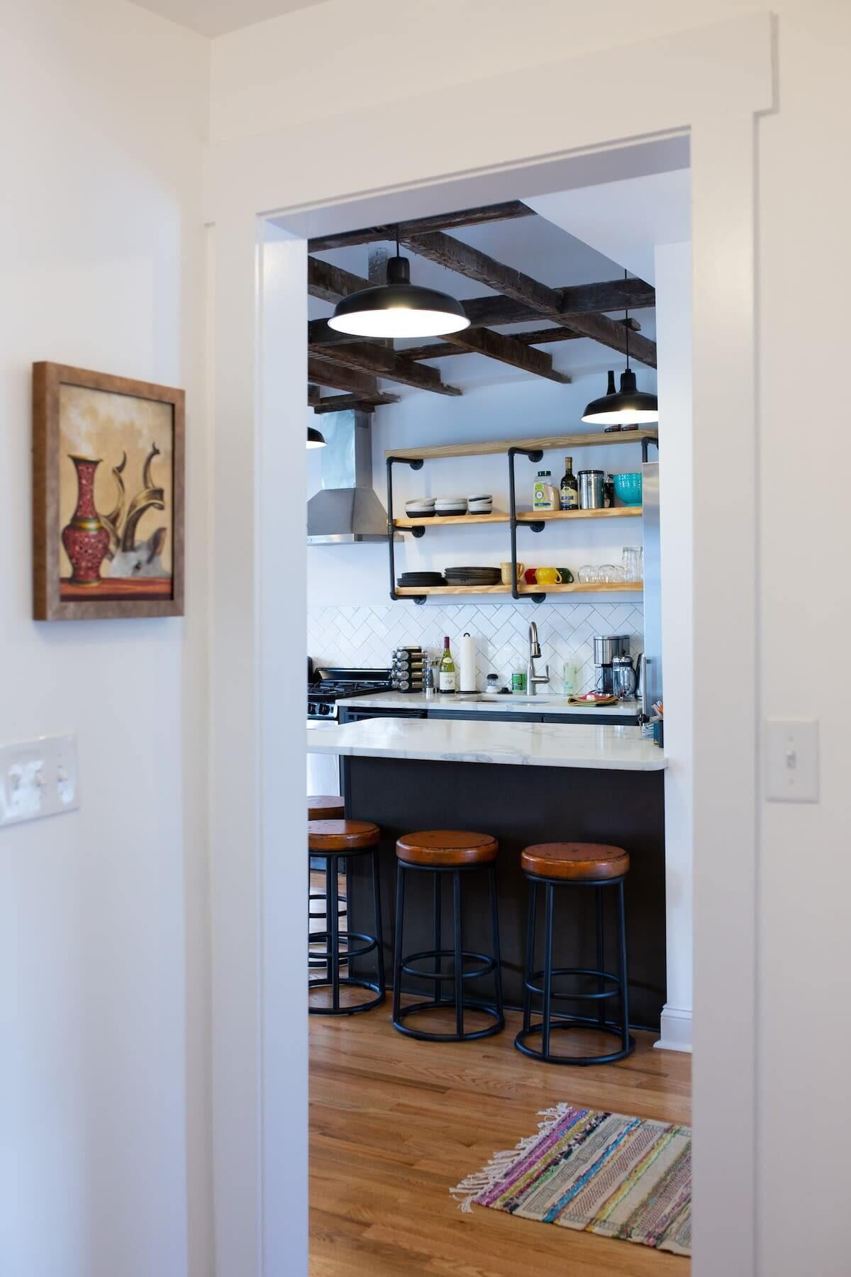 A modern kitchen with a white countertop, black bar stools, and wooden beams on the ceiling.