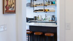 Une cuisine moderne avec un plan de travail blanc, des tabourets de bar noirs et des poutres en bois au plafond.