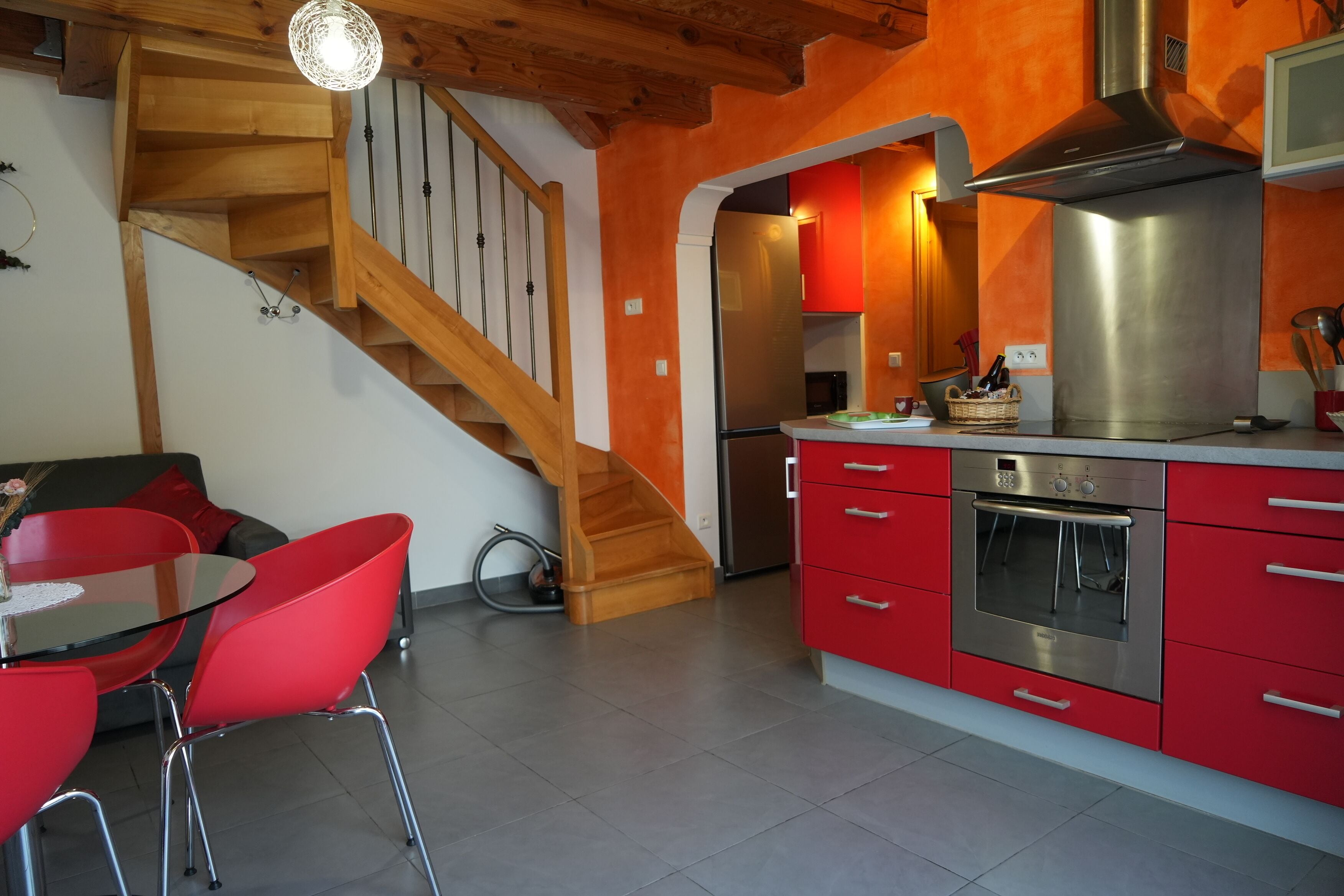 Une cuisine moderne avec des meubles rouges, des appareils en acier inoxydable et un escalier en bois.