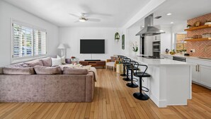 A modern kitchen with a central island, bar stools, and a dining area with a sofa and coffee table. - Rove Travel | Sunny Vista | Heated Pool & Firepit (West Palm Beach)